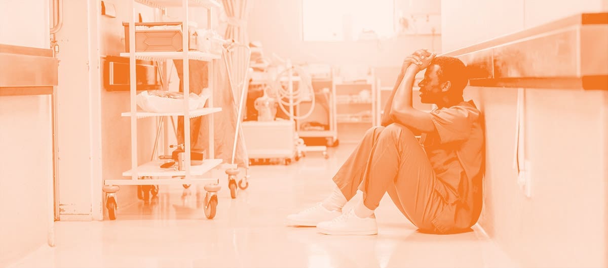 A distressed healthcare worker in scrubs sitting against the wall with head in hands