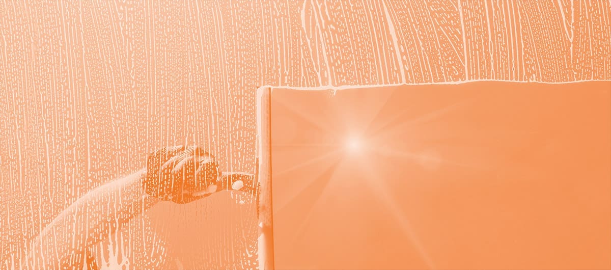 A hand cleaning a soapy window with the sun beaming through