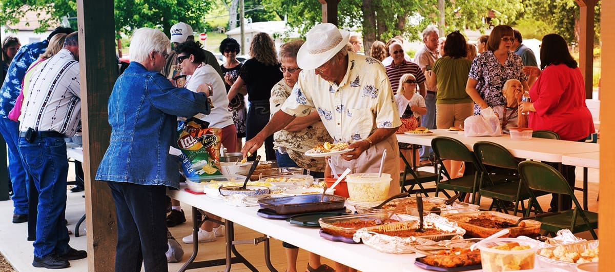 Group of people socializing and scooping food onto their plates at an outdoor gathering