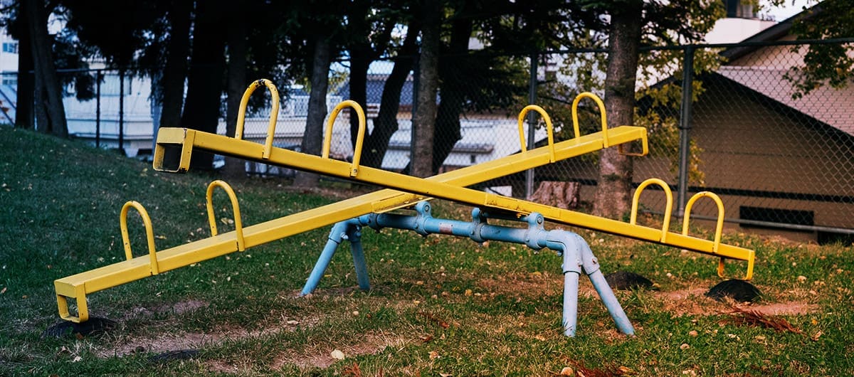 Two side by side yellow seesaws on blue piping, touching the ground at opposite ends
