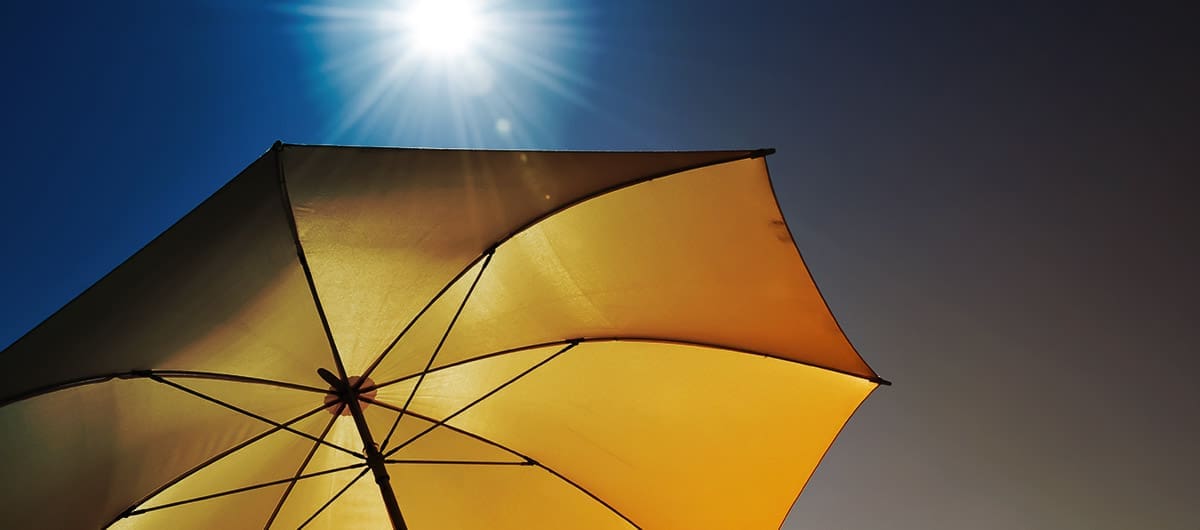 The under side of a yellow umbrella with a glaring sun in the background