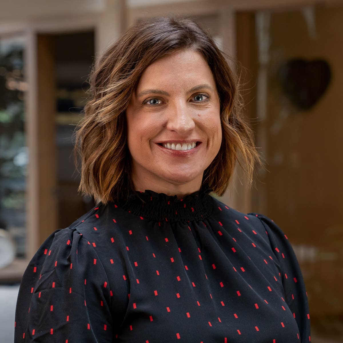Headshot of a smiling woman with short brunette hair, dressed in corporate attire in front of a blurred background