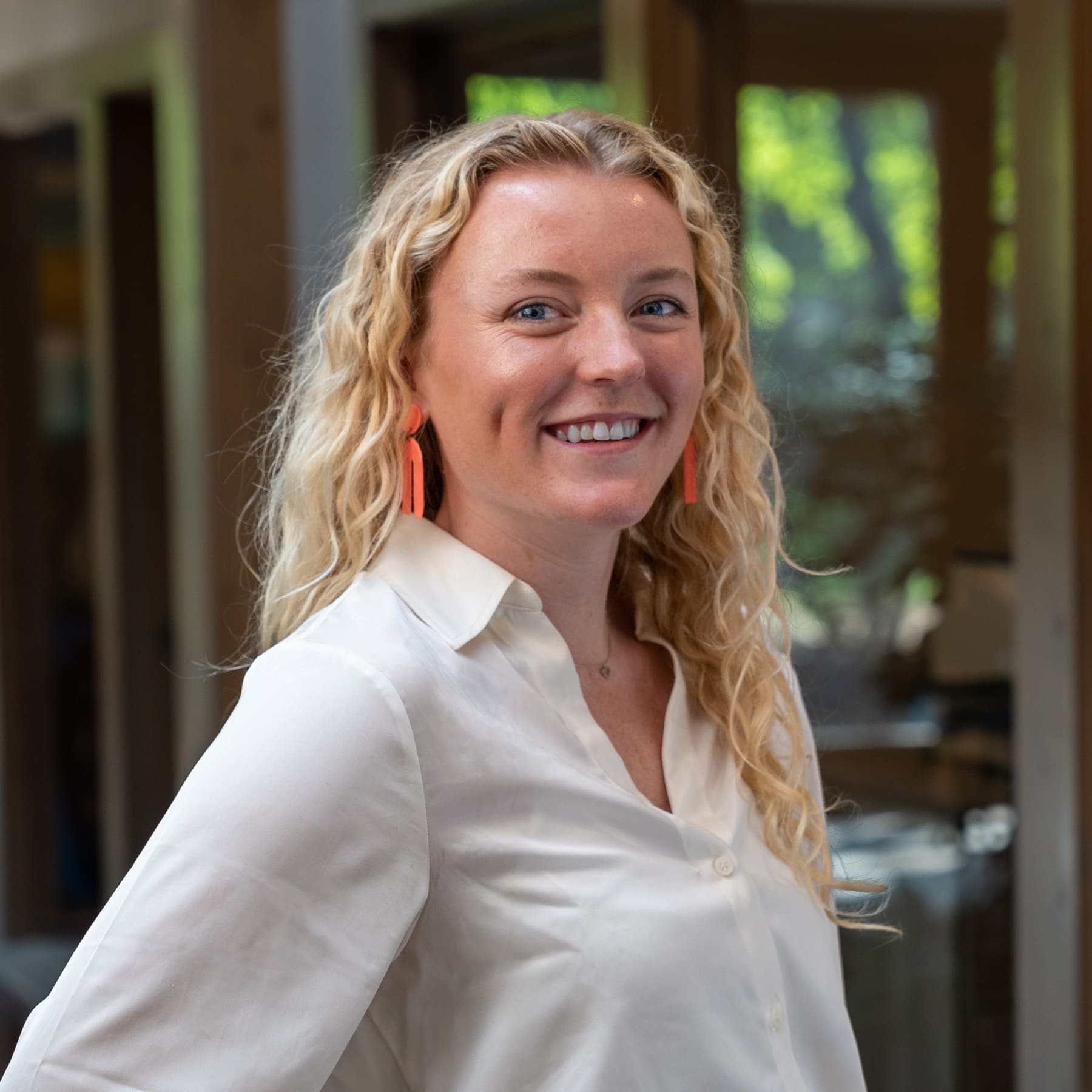 Headshot of a smiling young woman with blonde, curly hair dressed in corporate attire in front of a blurred background