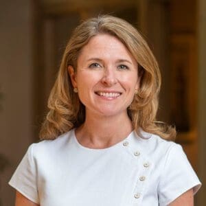 Headshot of a smiling middle-aged woman with light hair dressed in corporate attire in front of a blurred background