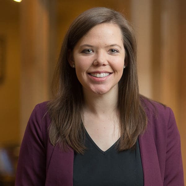 Headshot of a smiling woman with brunette hair dressed in corporate attire in front of a blurred background