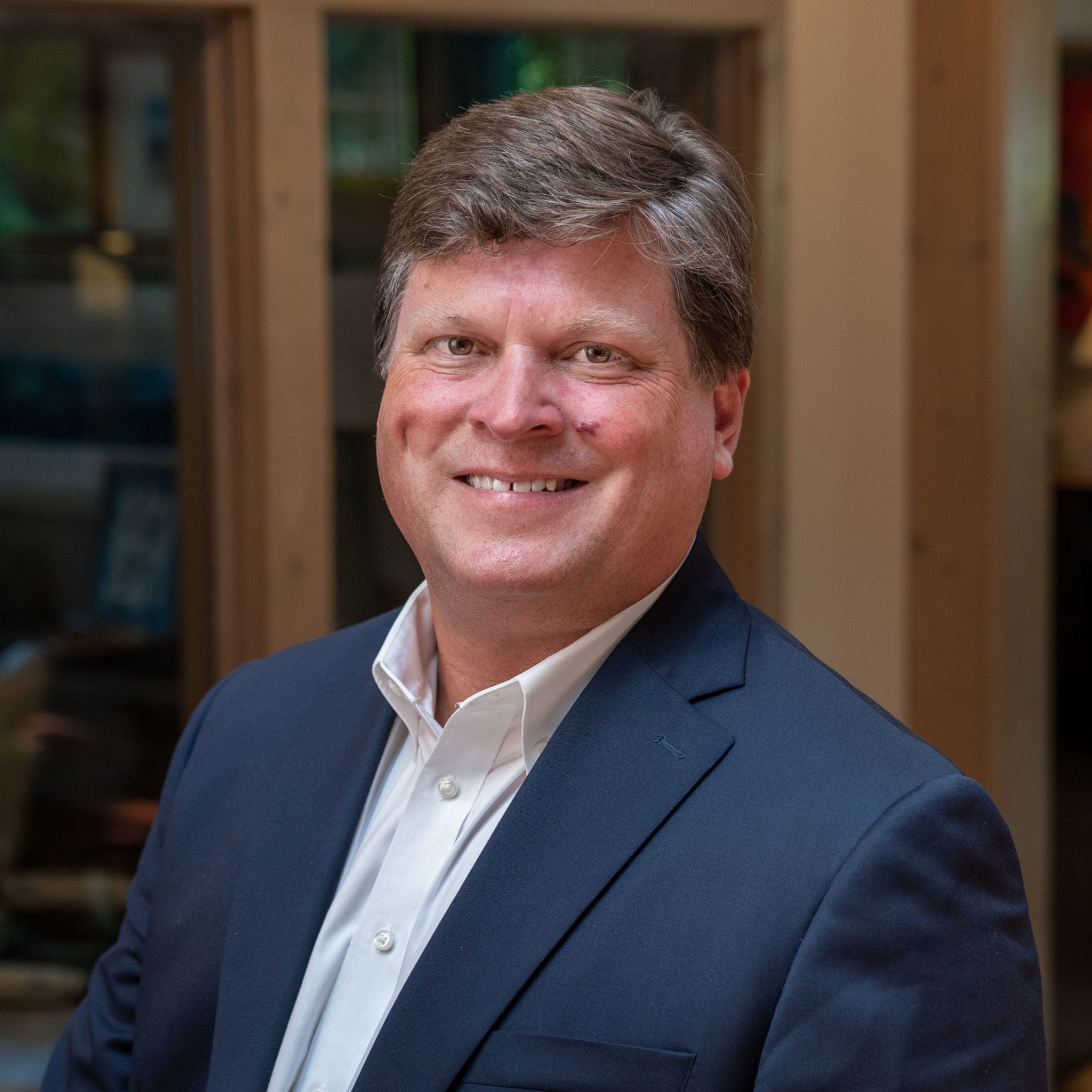 Headshot of a smiling man with light brown hair, dressed in a blazer in front of a blurred background