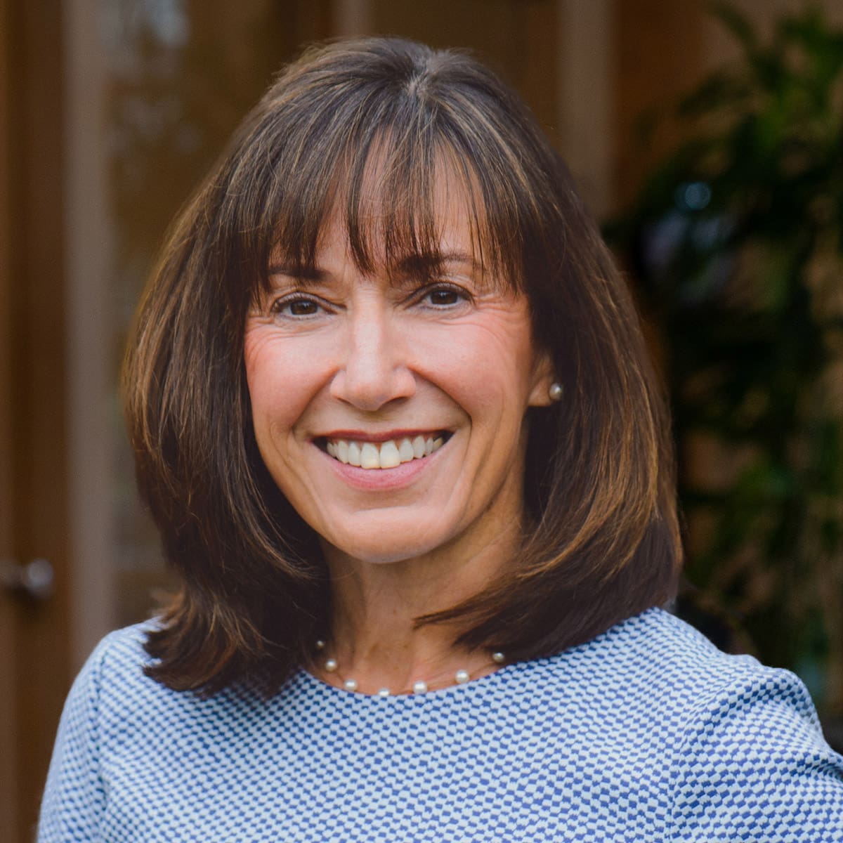 Headshot of a smiling woman with short, brunette hair dressed in corporate attire in front of a blurred background