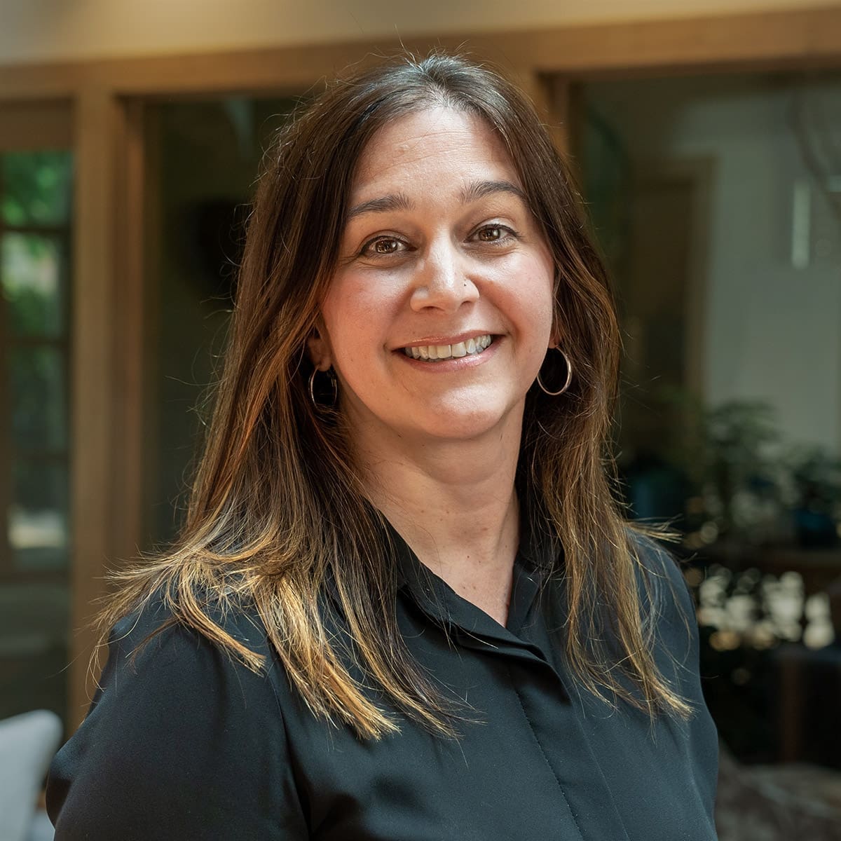 Headshot of a smiling woman with brunette hair dressed in corporate attire in front of a blurred background