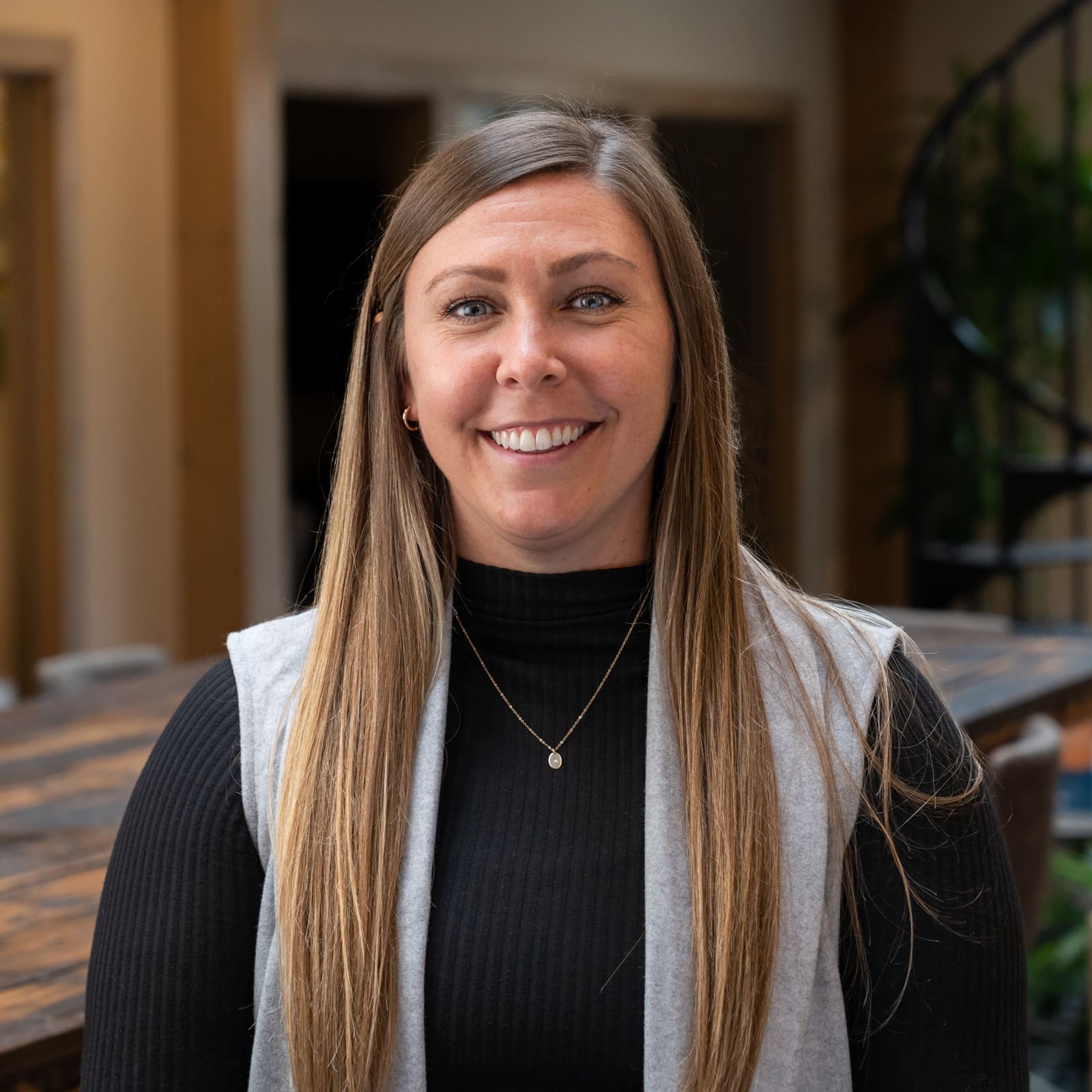 Headshot of a smiling young woman with long brunette hair dressed in corporate attire in front of a blurred background
